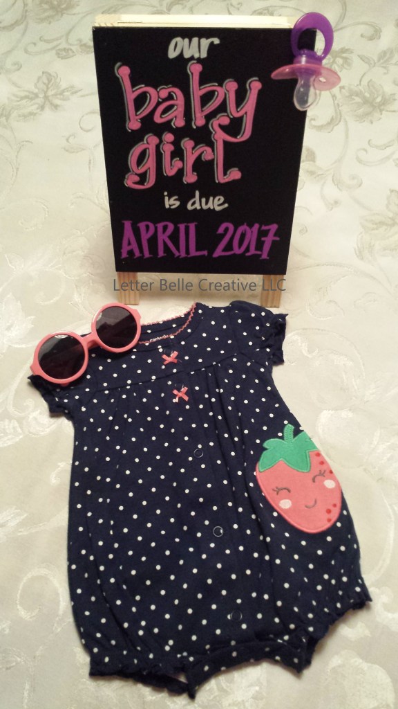 Pregnancy announcement. Small chalkboard with pink & purple hand lettering: our baby girl is due April 2017. Pictured with strawberry outfit & pink sunglasses

Letter Belle Creative