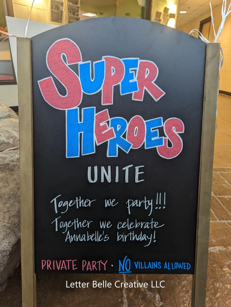 Chalkboard sign with red, white& blue hand lettering: Super Heroes unite! Together we party!!! Together we celebrate Annabelle's birthday!  Private Party. NO villians allowed

Letter Belle Creative