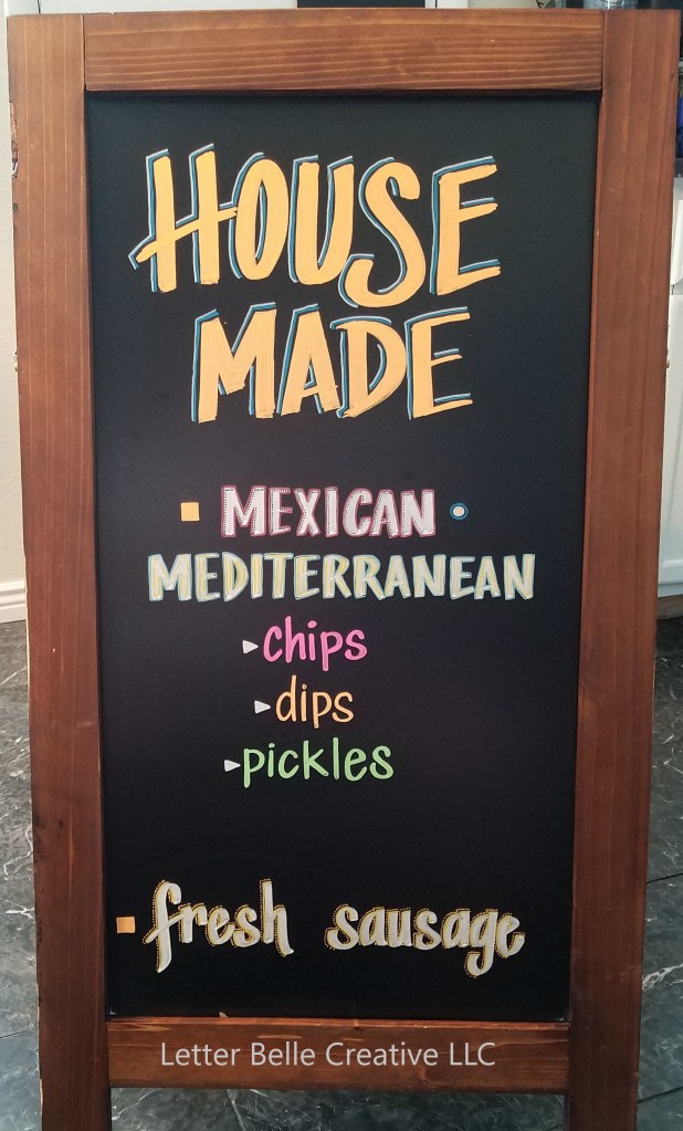 Framed chalkboard. Colorful hand lettering: House made. Mexican-mediterranean chips, dips, pickles. Fresh sausage

Letter Belle Creative