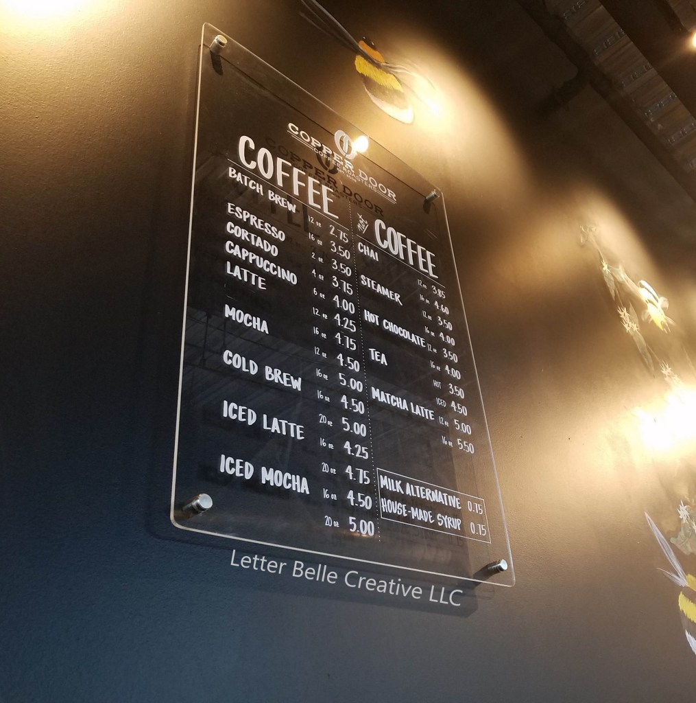Clear acrylic coffee shop menu for Copper Door Coffee Roasters mounted on black wall. White hand lettering listing coffee & not coffee items. Location: Denver Botanic Gardens on York Street

Letter Belle Creative