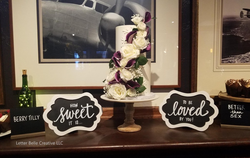 2-tier wedding cake flanked by two white-framed chalkboards with white hand lettering: How sweet it is... to be loved by you! Cupcakes with tags: Berry Tilly & Better than Sex

Letter Belle Creative
